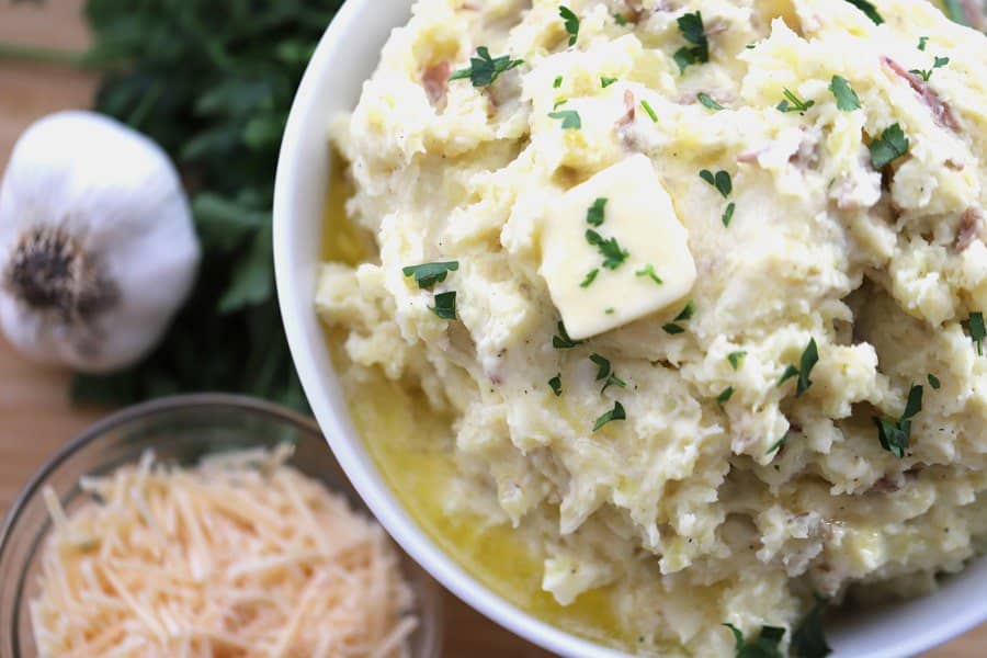 Side dish of mashed potatoes in a bowl, topped with butter and fresh herbs.