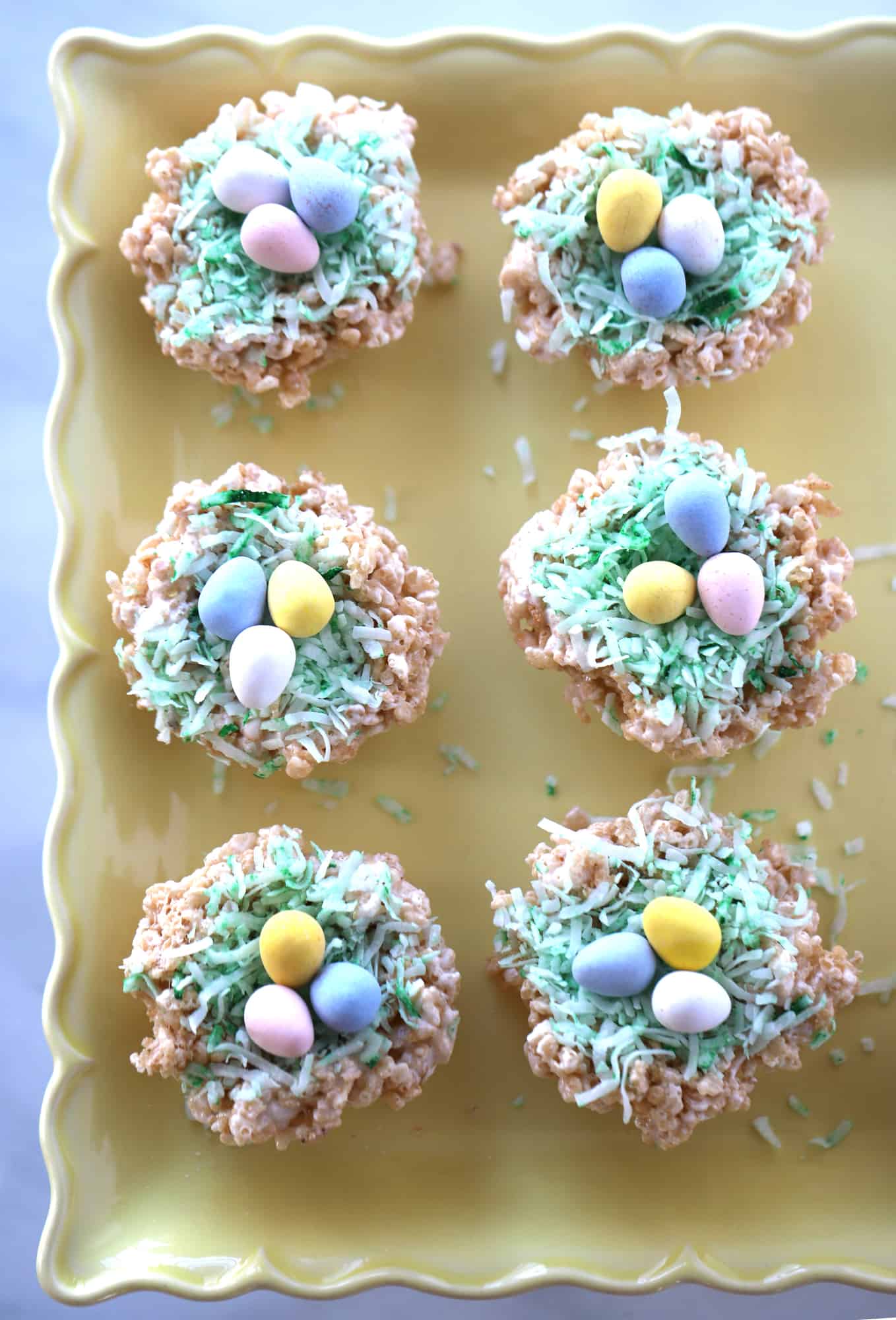 rice krispie easter nests on a serving plate, adorable easter rice krispie treats topped with coconut grass and egg candies.