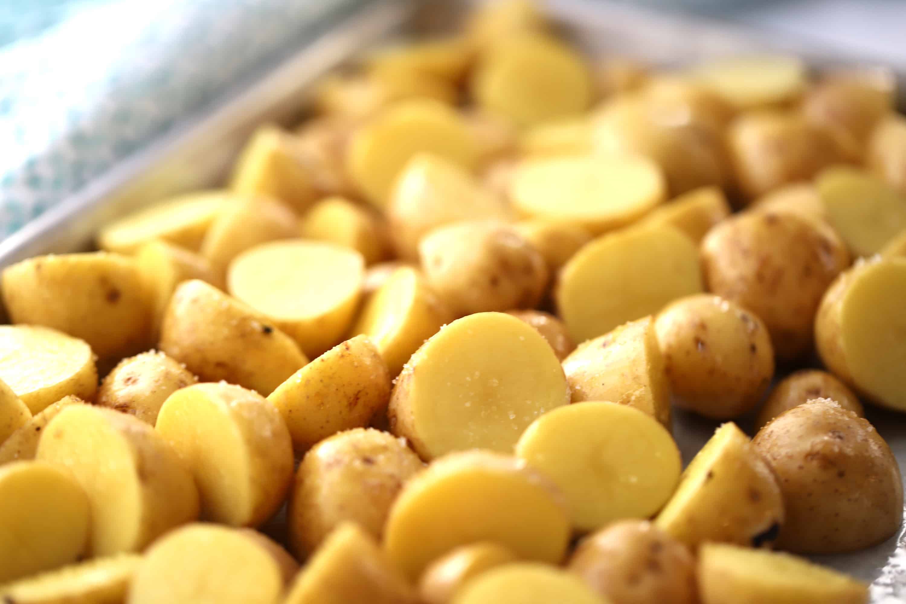 Small potatoes cut in half and spread out on a baking sheet.