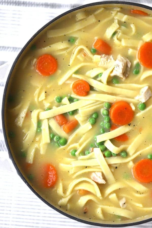 homemade chicken noodle soup with pea and carrots in a large pot.