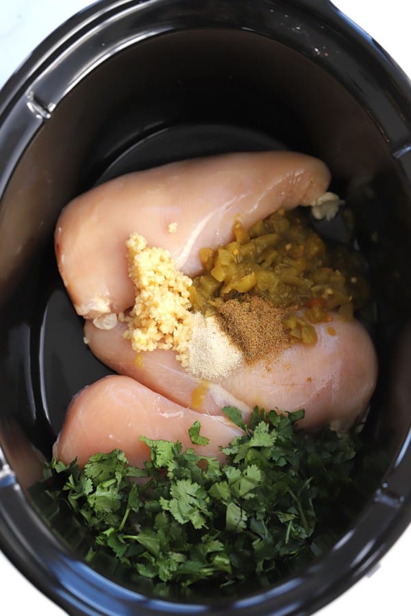 raw chicken breast, cilantro, chopped garlic and spices in a crockpot ready to make crock pot cilantro lime chicken.