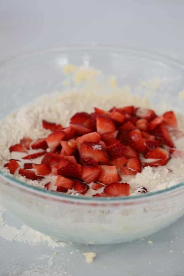 A glass mixing bowl full of scone dough with diced strawberries.
