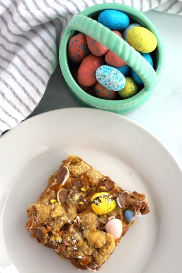 a Cadbury Cookie Bar square on a small white plate with a mini basket of Cadbury mini eggs beside it, cadbury chocolate bars recipe.