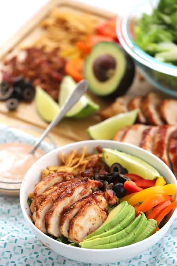 BBQ grilled chicken salad in a serving bowl with more fresh ingredients in the background.