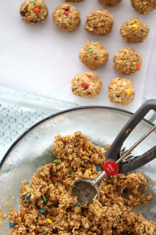A large mixing bowl full of peanut butter and oats mixture with a cookie scoop scooping out power balls onto a baking sheet.