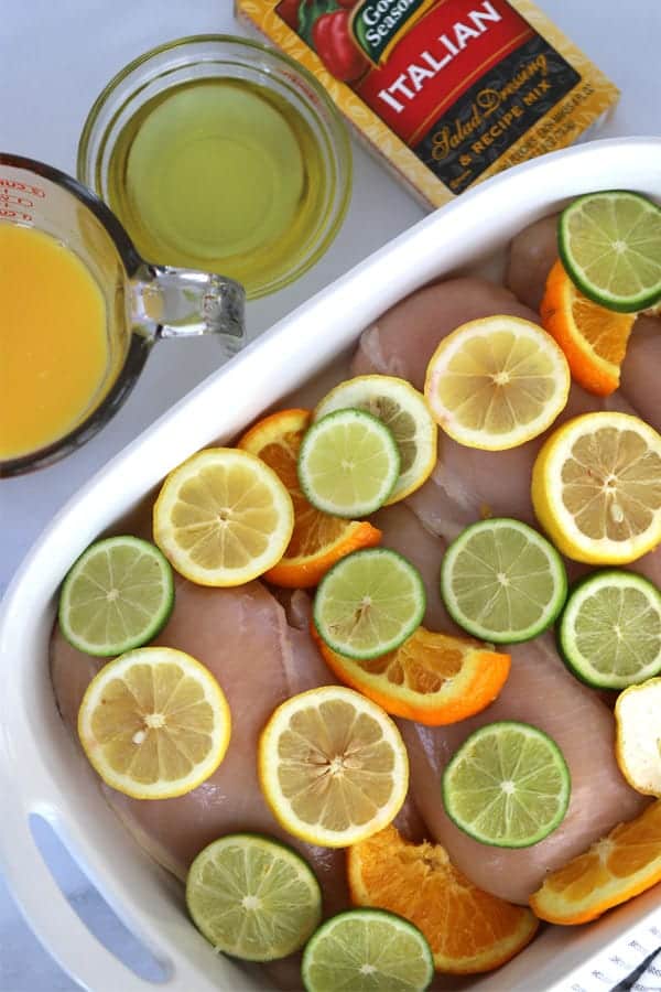 Chicken breasts in a baking dish topped with Citrus chicken marinade and sliced oranges, lemons and limes.