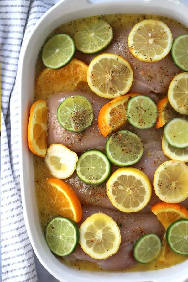 marinating Chicken breasts in a baking dish in a citrus marinade for chicken, topped with seasoning and slices of limes, lemons and oranges.