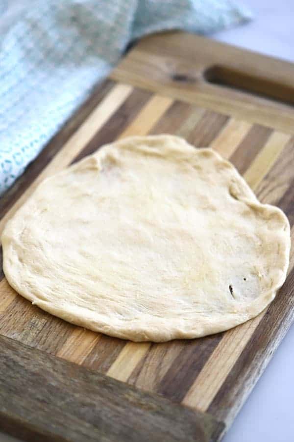 A cutting board with a round of flattened pizza dough.