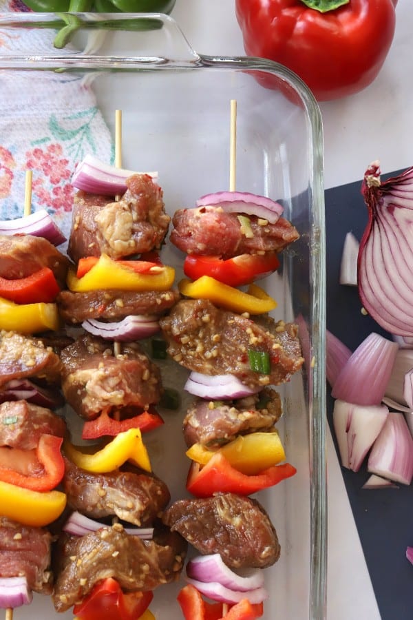 Asian flavored beef kabobs in a glass baking dish ready to cook.