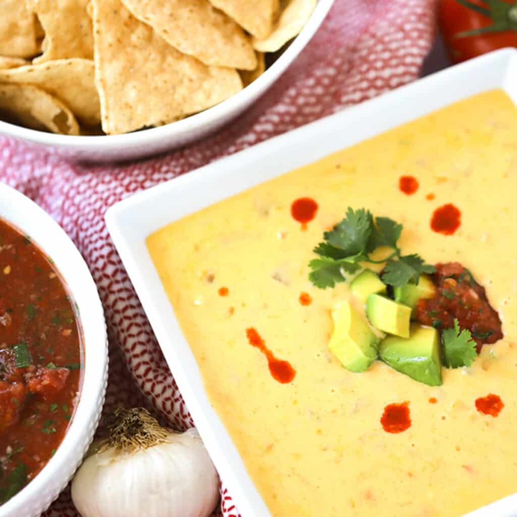 Cheddar Queso Dip with chips on the side and hot sauce with avocado garnish, quick appetizer recipes.