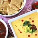 Cheddar queso dip in a bowl served with chips on the side