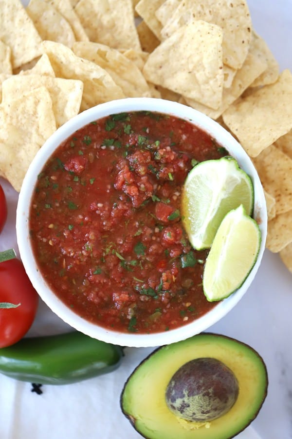 fresh salsa ingredients in a serving bowl with chips and avocado