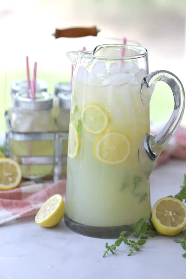 Mint lemonade in a tall clear pitcher with lemons and mint as garnish