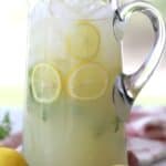 Mint lemonade in a clear pitcher with mint leaves and sliced lemons