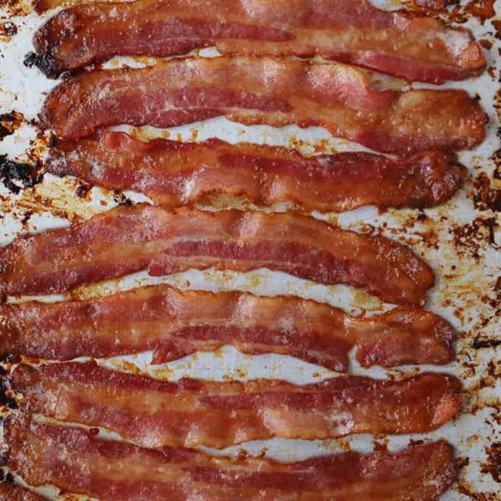 Candied bacon strips cooked and resting on a sheet tray.