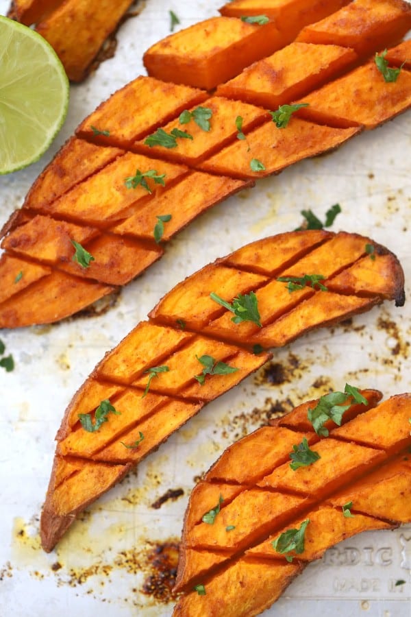 Roasted sweet potatoes that have been cut in half and scored, then topped with fresh herbs.