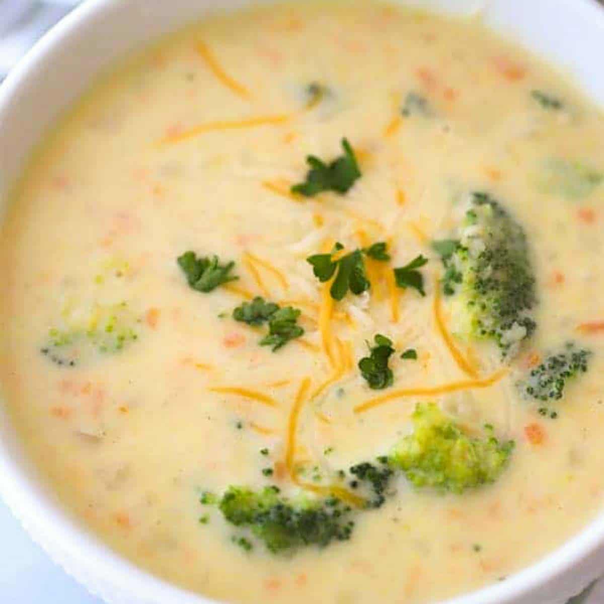 creamy Broccoli Potato cheese soup REcipe in a white bowl with broccoli on top