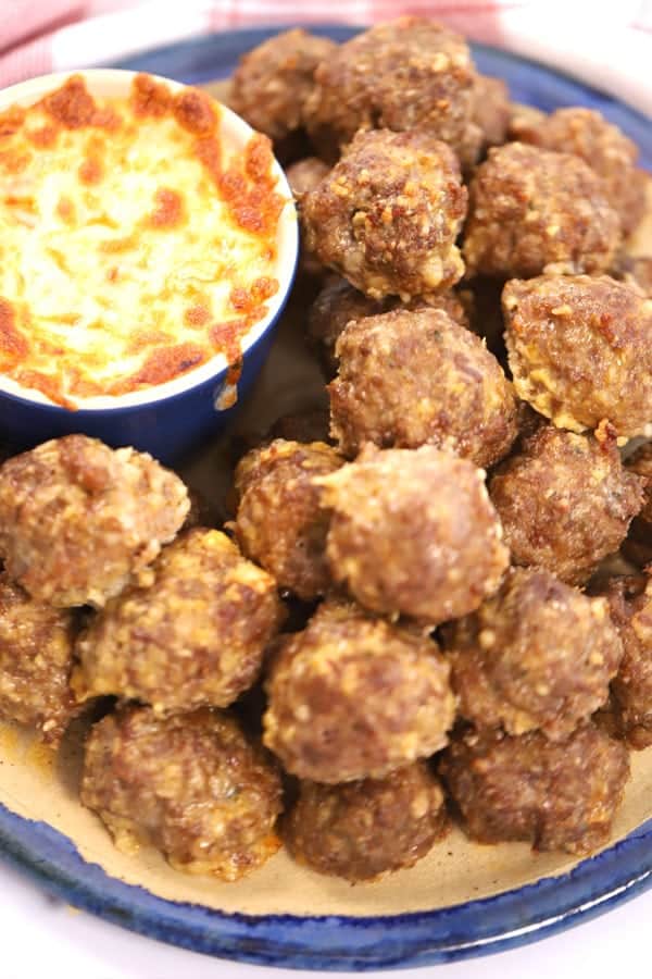 A large serving bowl full of spicy meatballs with a side of dipping sauce.