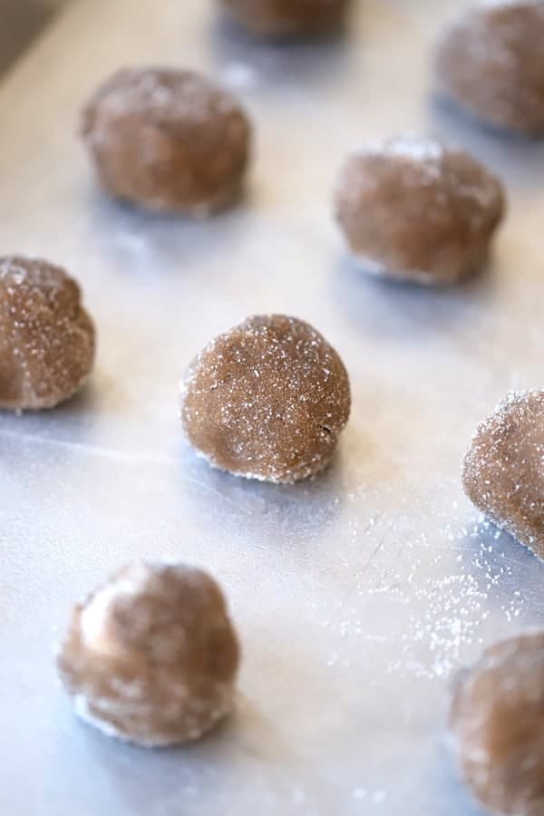 Little balls of ginger snaps cookies dough on a baking sheet dusted with sugar before baking.