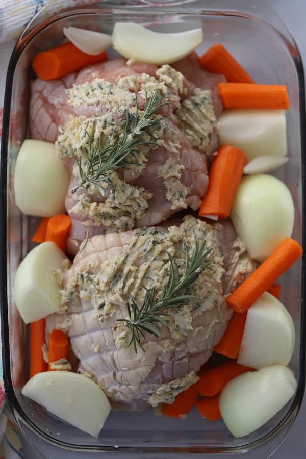 Raw turkey breast covered with herbed butter, ready to bake in the oven with carrots and onions in a baking dish