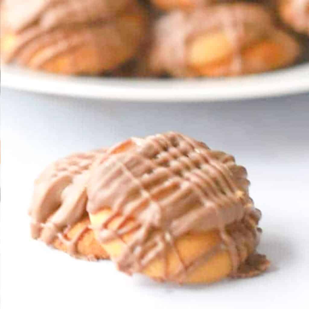 A couple of chocolate and caramel drizzled nilla wafers staked on top of each other with a full plate of them in the background.