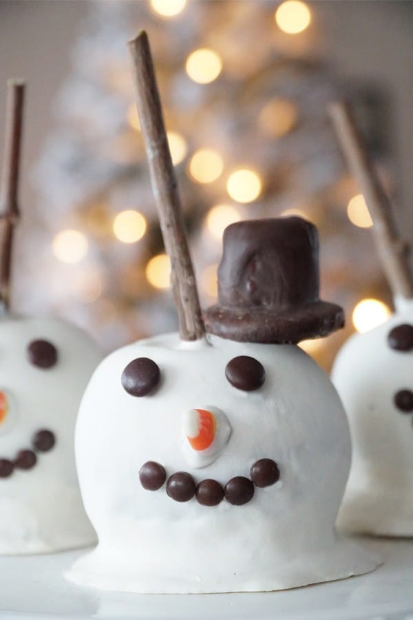 A homemade caramel apple decorated to look like a snowman, with a top hat and candy face. Christmas apples. Christmas candy apples.