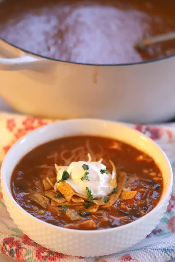 A white serving bowl full of this enchilada soup recipe, topped with tortilla strips, sour cream and cilantro.