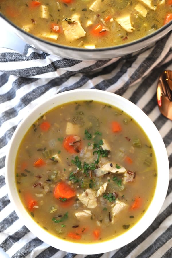 Turkey and wild rice soup in a white serving bowl with a large stock pot full of soup to the side. Turkey soup recipe with rice. Turkey wild rice soup recipe. Turkey soup recipes with rice.