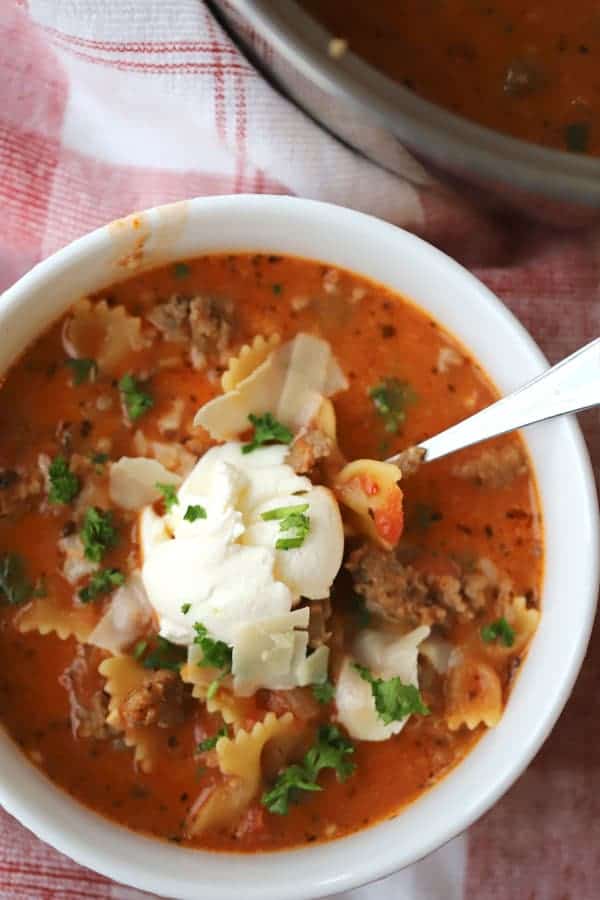 lazy lasagna soup in a bowl, topped with ricotta cheese, parmesan cheese, and parsley.