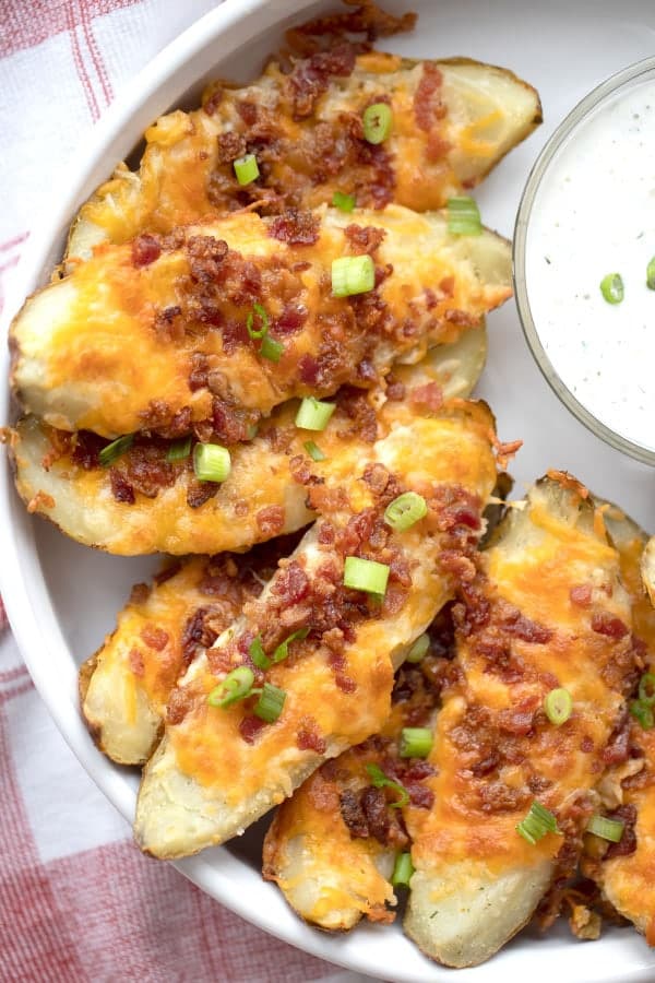 Loaded baked potato skins on a serving dish, topped with sliced green onions. recipe for loaded potato skins. 