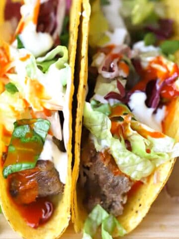crockpot shredded beef tacos, shredded beef in a hard taco shell, covered with cheese, sour cream and taco toppings