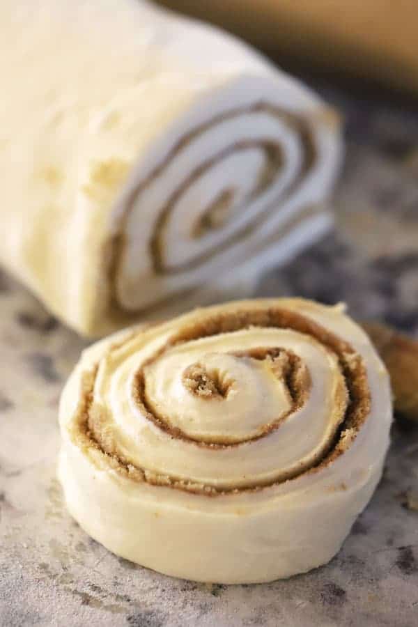 Unbaked caramel cinnamon rolls in a roll with a slice cut from it.