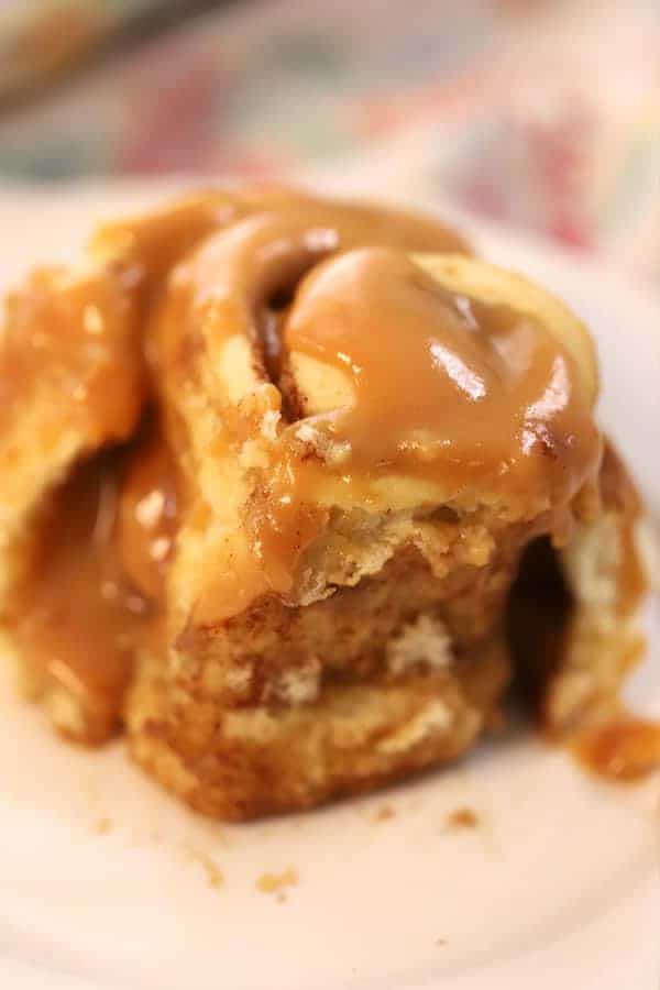 A cinnamon roll covered in caramel sauce on a small plate.