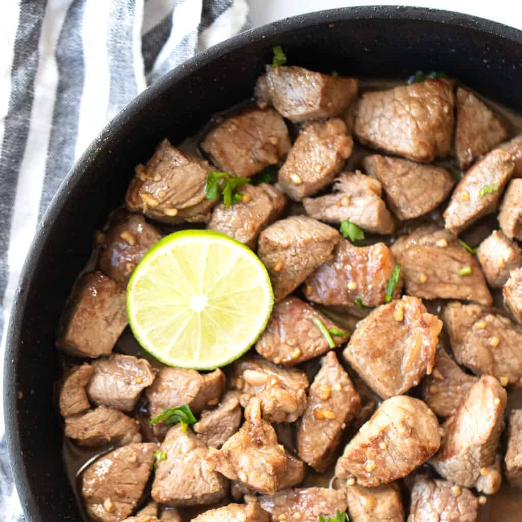 Honey garlic steak bites in a cast iron skillet with a fresh lime.