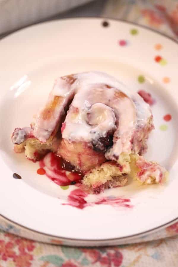 Berry sweet roll on a plate with lemon icing.