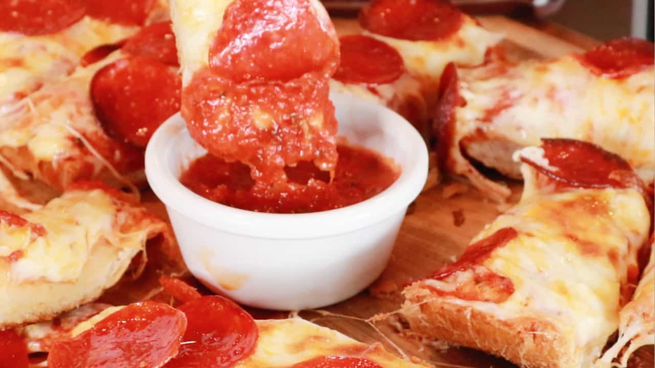 A slice of pepperoni pizza bread being dipped into marinara sauce.