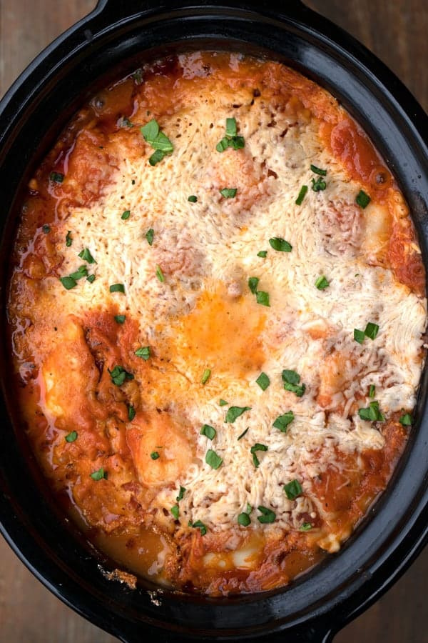 cooked crockpot lasagna with ravioli topped with parsley. crock pot lazy lasagna  cooked with melted cheese on top. 