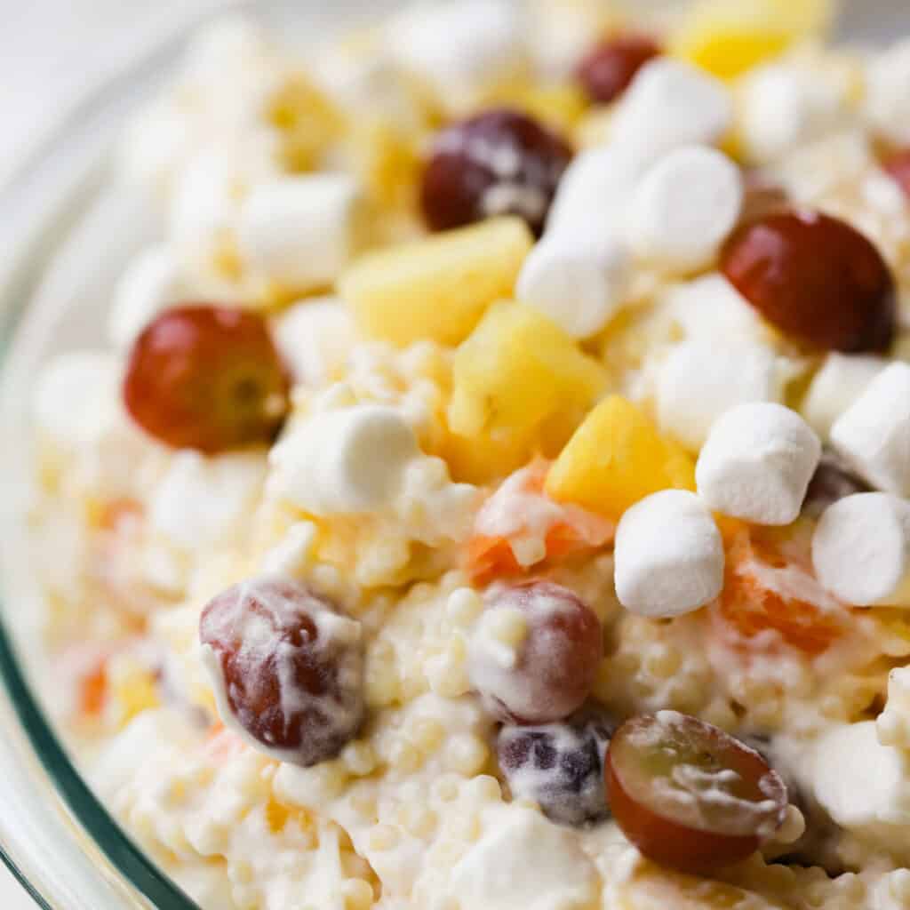 A glass bowl full of this recipe for easy frog eye salad, full of grapes, mini marshmallows, and more.