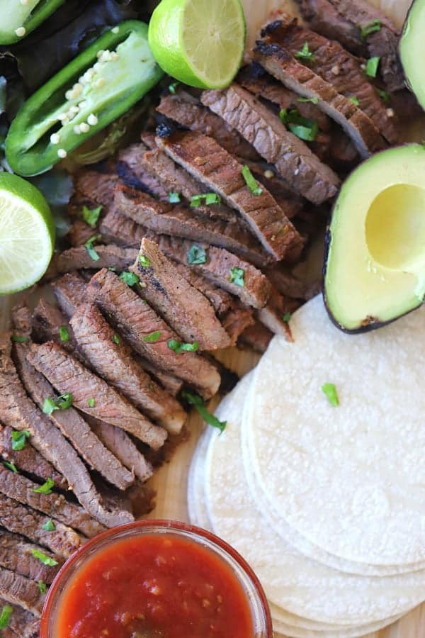 carne asada marinade recipe with taco toppings on a cutting board, carne asada translation, carne asada marinade recipe, quick carne asada marinade.