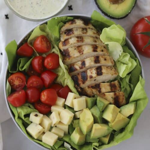 Healthy grilled chicken salad in a bowl with a side of pesto ranch.