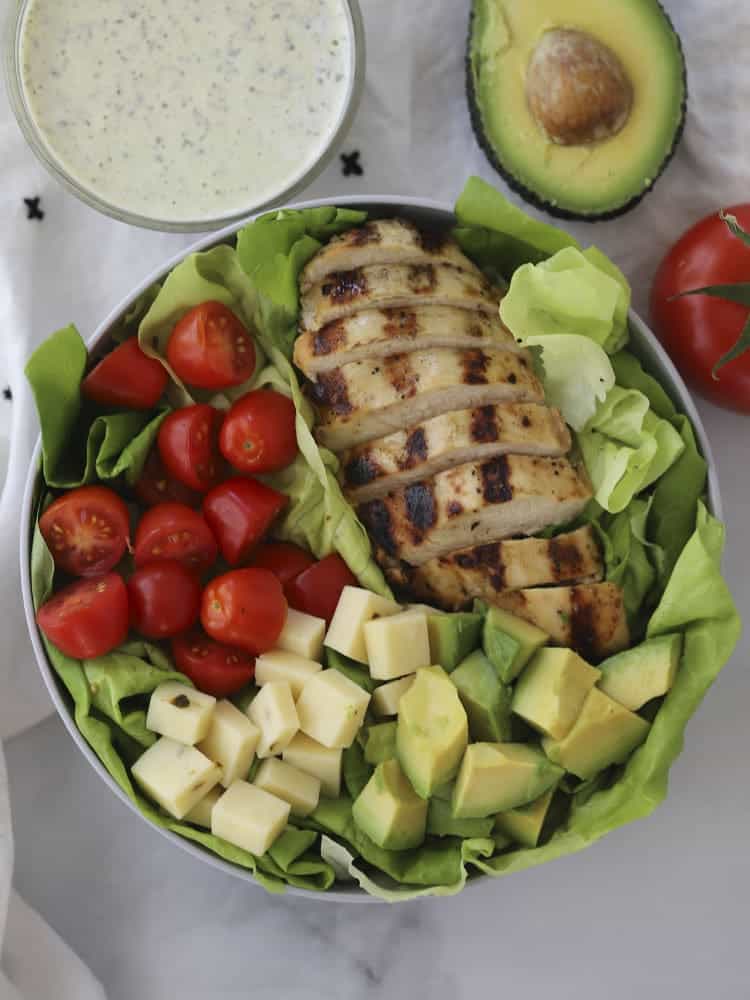 Healthy grilled chicken salad in a bowl with a side of pesto ranch.