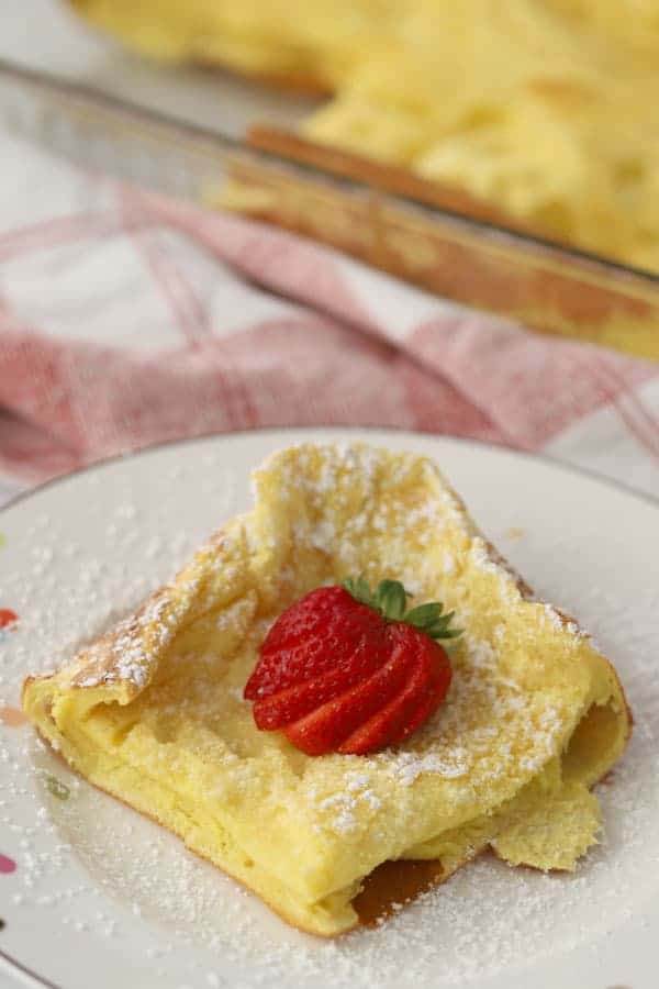 German Pancakes on a plate topped with powdered sugar and a fresh strawberry. The best german pancake recipe ever.