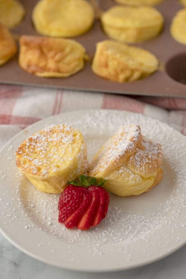 Individual sized Dutch baby pancakes on a small plate topped with powdered sugar and a fresh strawberry.