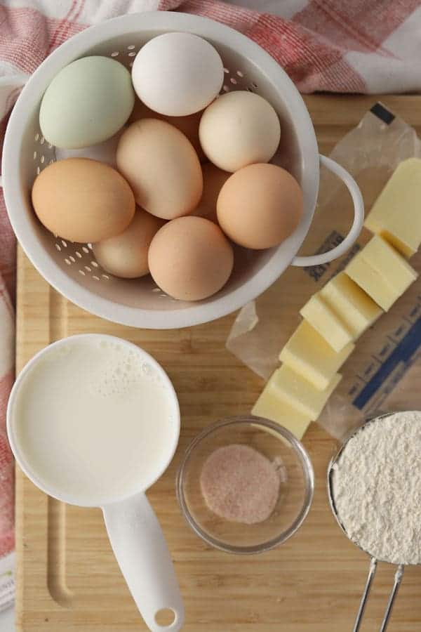 A photo showing the ingredients needed for how to make German Pancakes on a cutting board, including eggs, butter, milk, flour and salt.