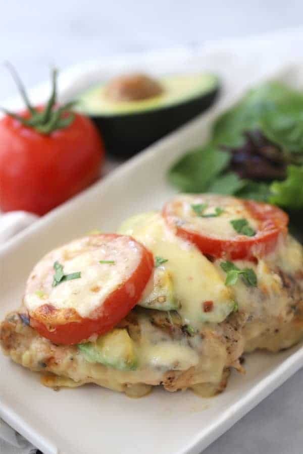 grilled california chicken on a white plate, topped with tomatoes, cheese and fresh herbs.