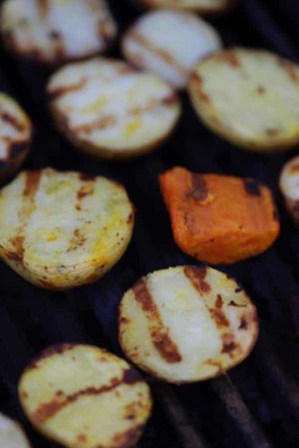 Sliced potatoes on a grill with grill marks on the top side.