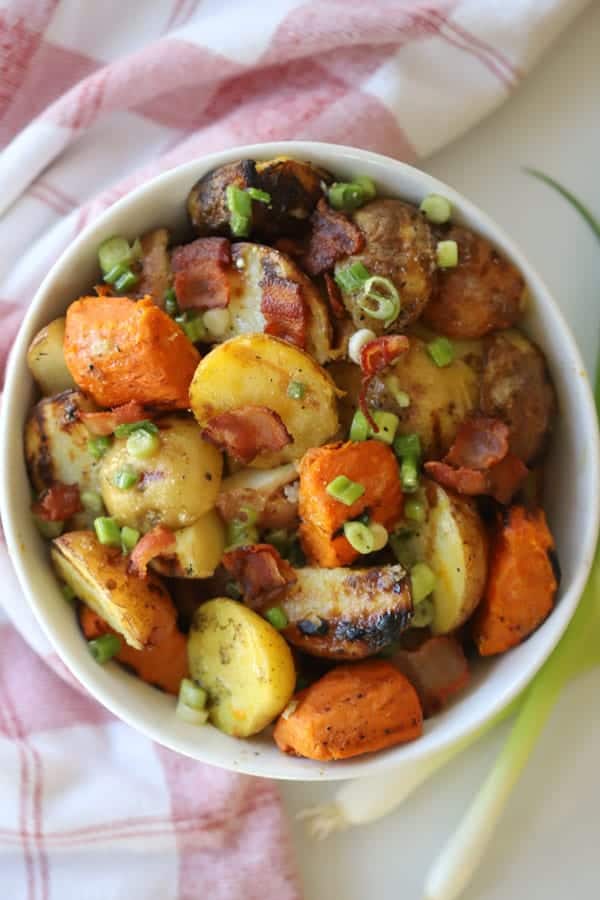 A white bowl full of potato salad made with grilled potatoes, bacon, green onions and dressing.