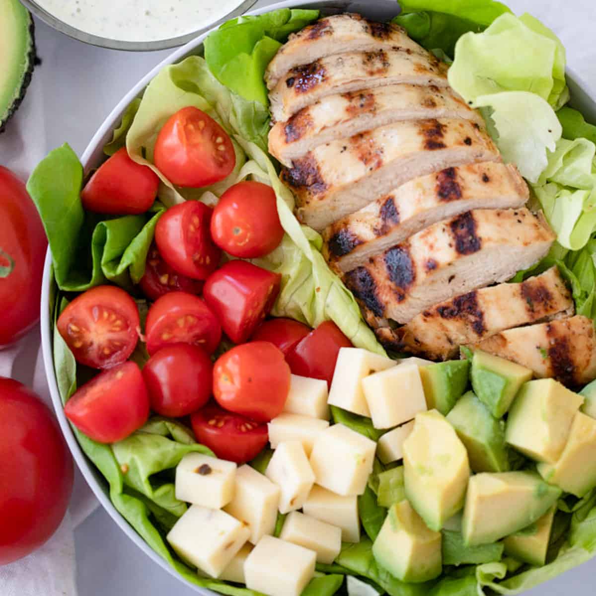 Healthy grilled chicken salad in a bowl with a side of pesto ranch.