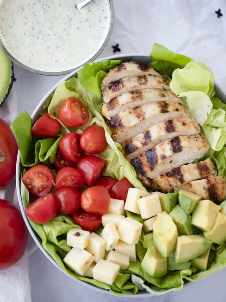 Healthy grilled chicken salad in a bowl with a side of pesto ranch; ranch dressing, marinade for chicken.