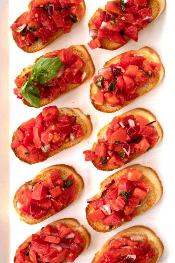 Tomato and basil bruschetta lined up on a serving platter.